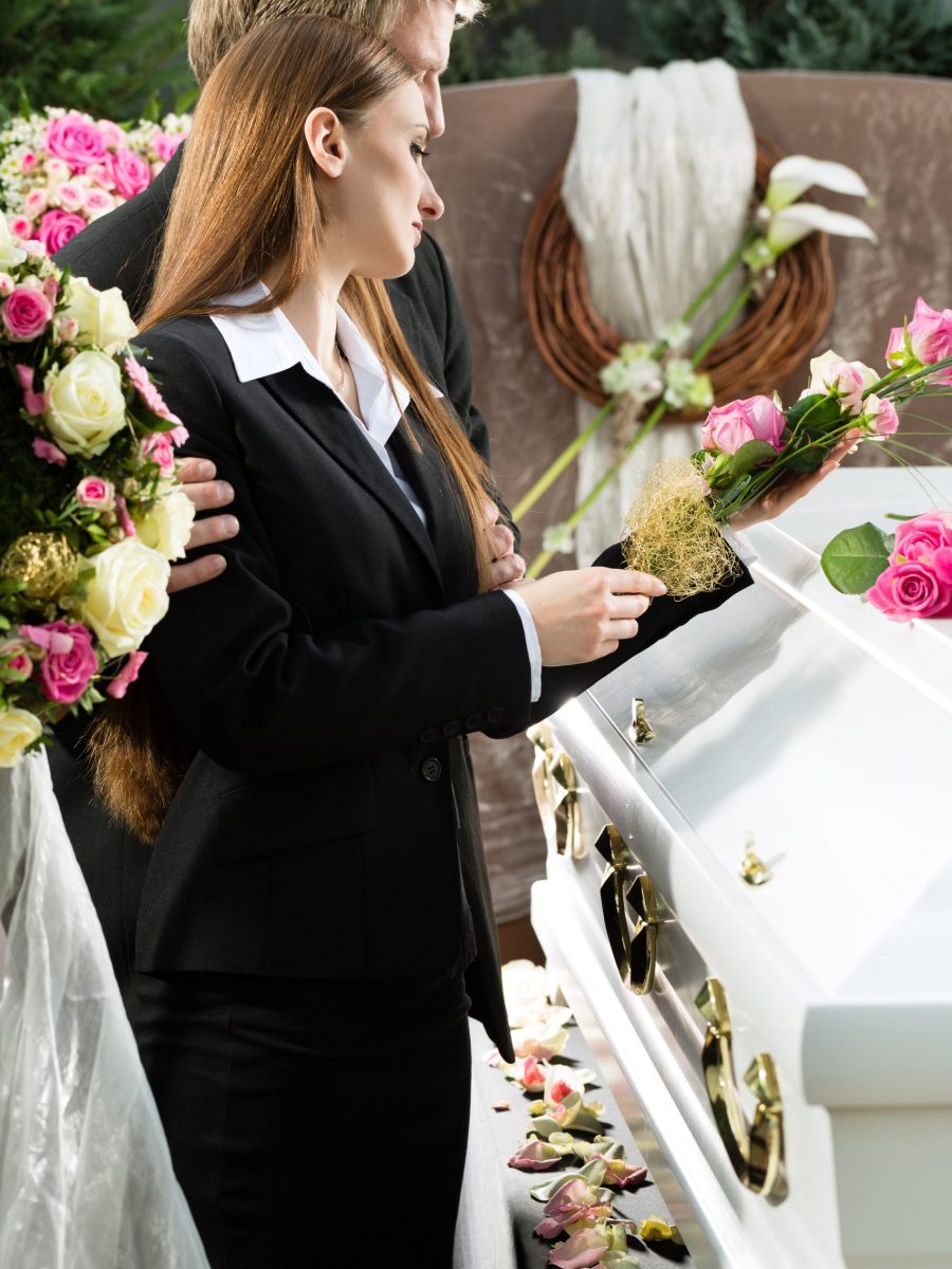 Mourning man and woman on funeral with pink rose standing at casket or coffin